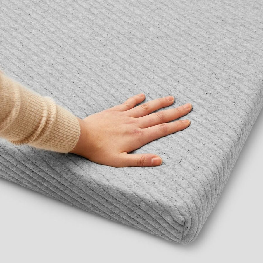 A hand pressing into the grey knit cover of the Casper Comfy Mattress Topper